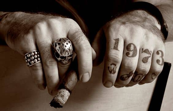 close up photo of tattooed hands holding cigar with big skull ring